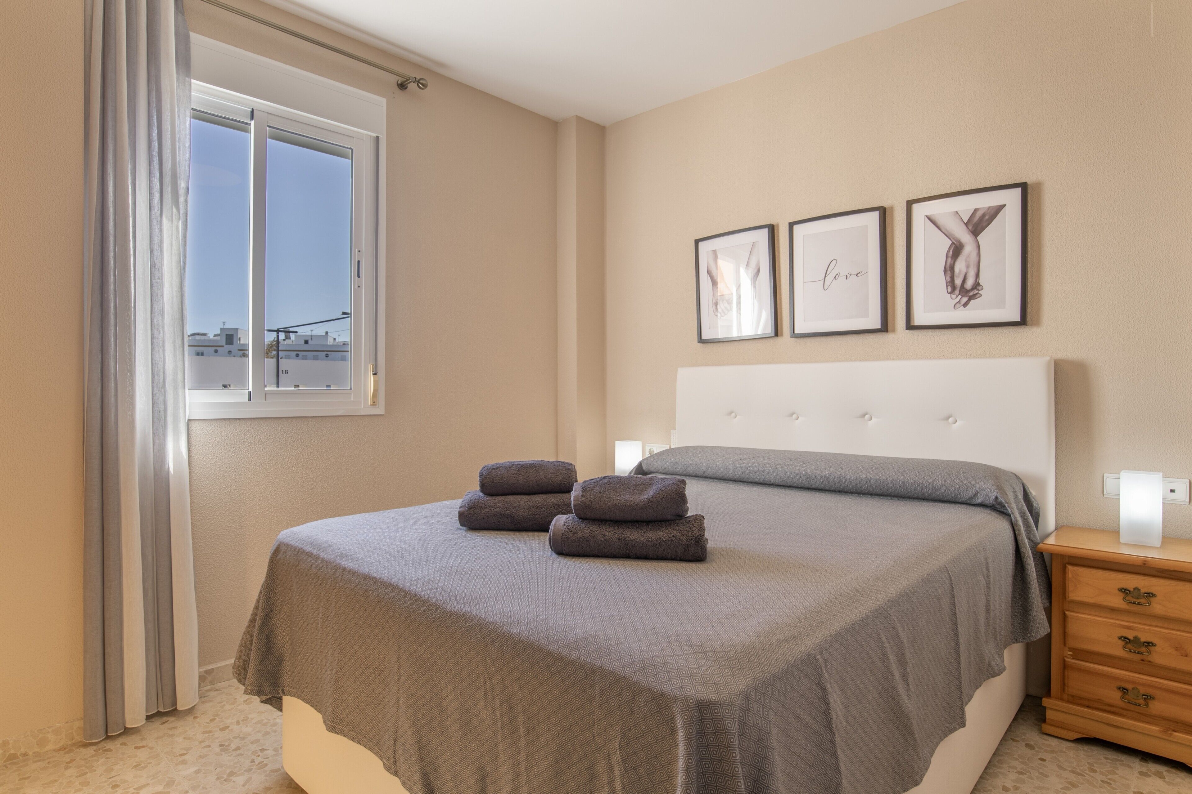 A bedroom with a bed, a window with curtains, and three framed pictures on the wall.