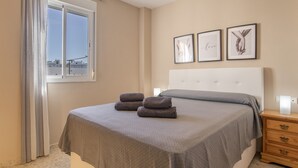 Ein Schlafzimmer mit einem Bett, einem Fenster mit Vorhängen und drei gerahmten Bildern an der Wand.