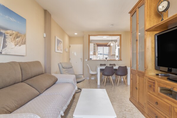 A living room with a sofa, a dining table with chairs, a TV, and a clock on the wall.