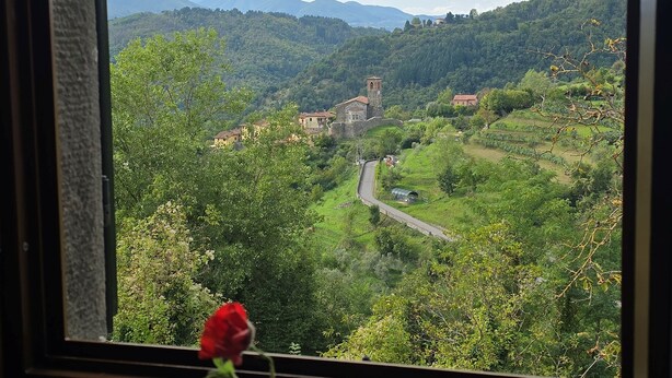 Une vue à travers une fenêtre sur une vallée, avec une route, une église et de la verdure.