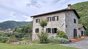 Une maison en pierre avec un toit en tuiles, de nombreuses fenêtres équipées de volets et un jardin bien entretenu.