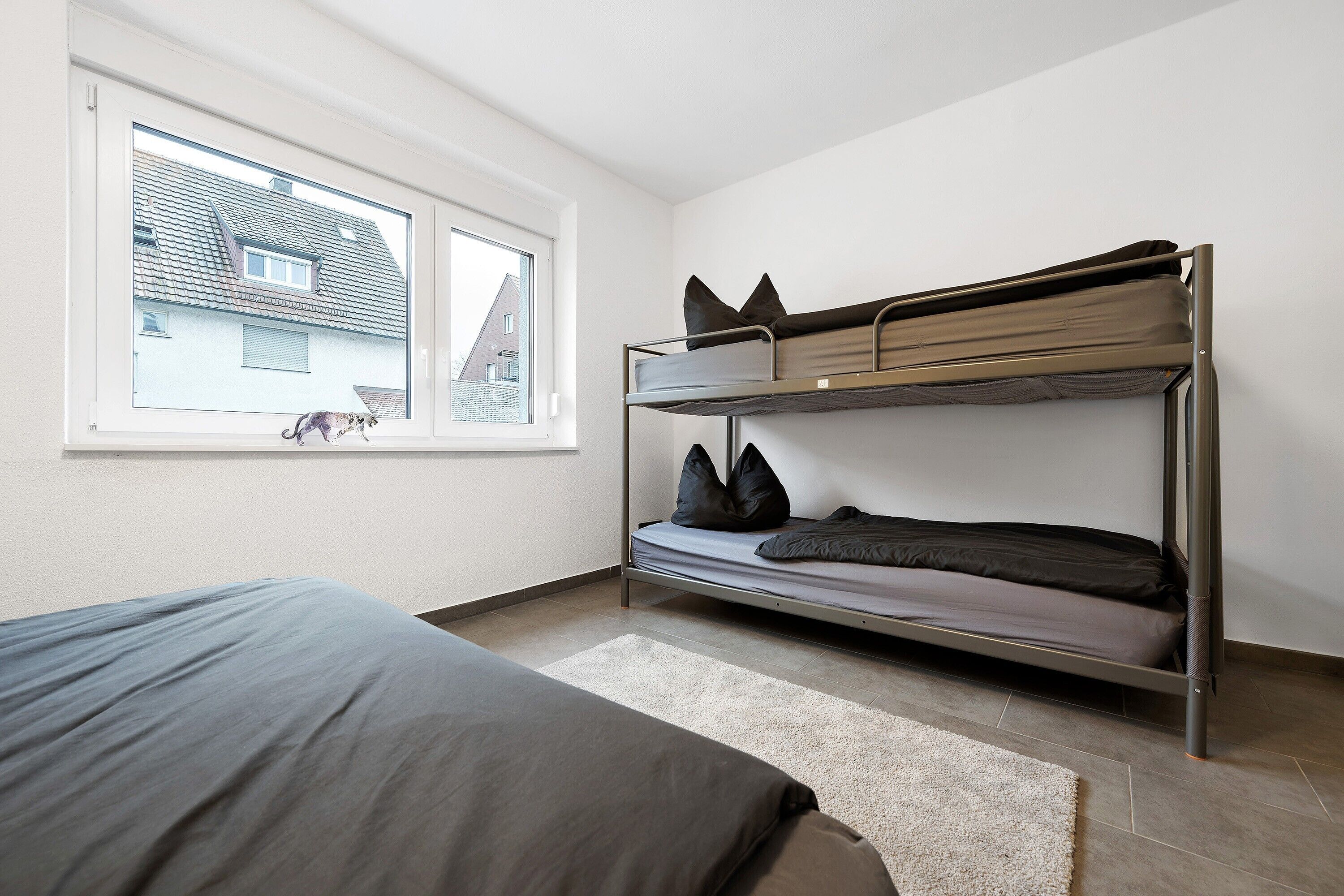 Ein Etagenbett mit Blick aus dem Fenster, ein Bett mit grauer Decke und ein weißer Teppich.