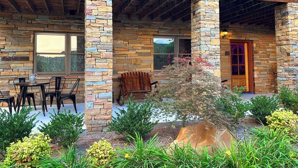 A stone building with a covered patio, outdoor seating, and a small garden. - Luminary Lodge: an Appalachian arcade of interactive inventions above the clouds (Sevierville)
