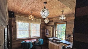 A wooden cabin interior with a dining area, kitchen, and large windows. - Luminary Lodge: an Appalachian arcade of interactive inventions above the clouds (Sevierville)