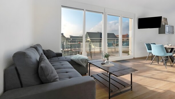 A modern living room with a grey sectional sofa, a small table, and a TV mounted on the wall.
