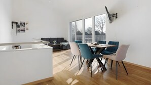 A modern interior with a dining area, a sofa, and large windows.