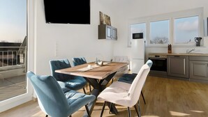A modern kitchen with a dining area, large windows, and a flat-screen TV.