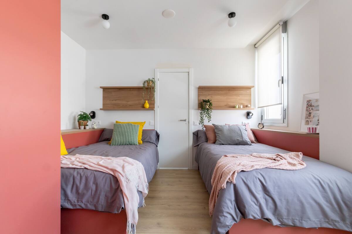 Une chambre moderne avec deux lits, des têtes de lit en bois et une petite fenêtre.