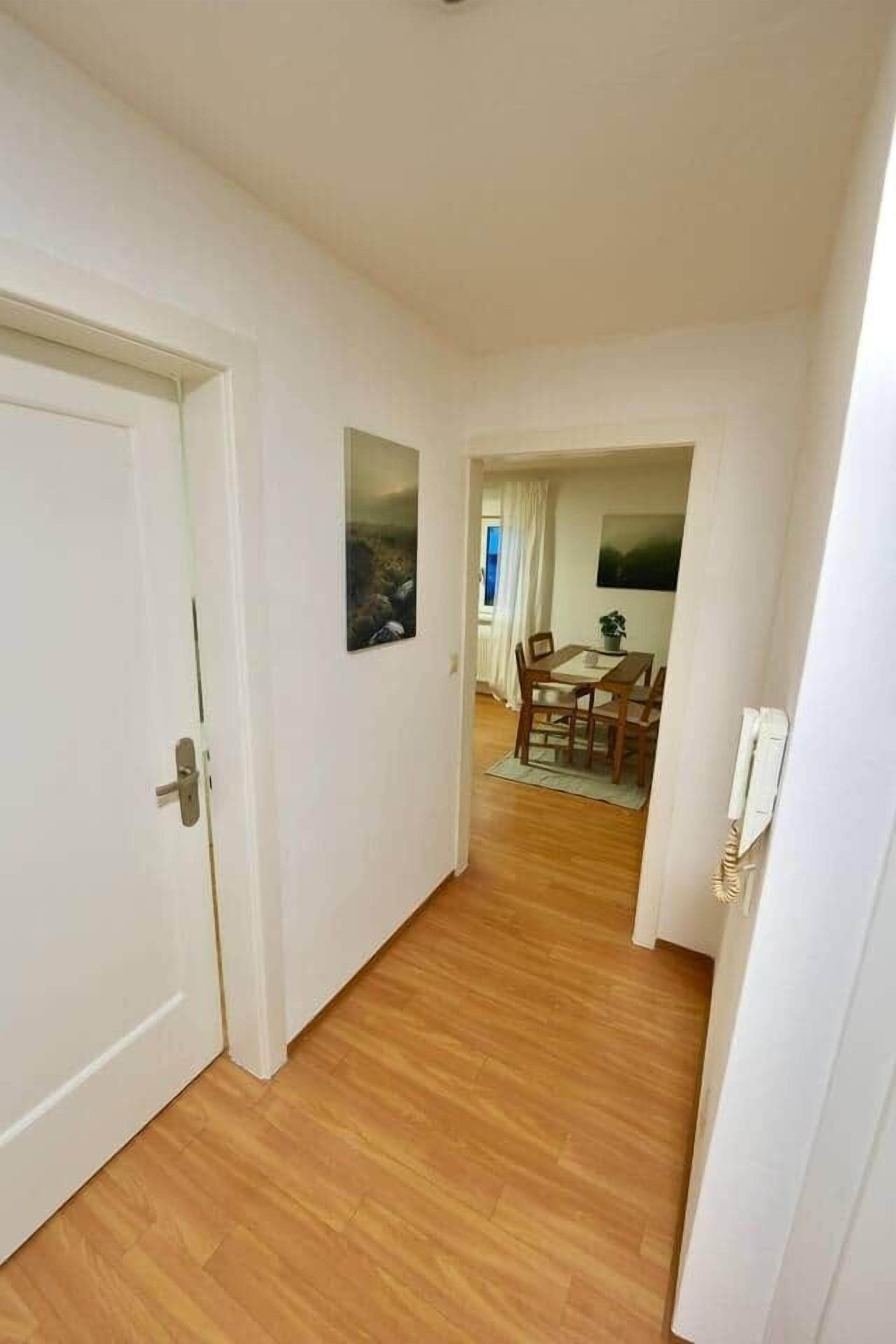 Un couloir avec un plancher en bois, un coin repas avec des chaises et une table, et une porte avec une poignée.