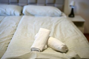 Un lit bien fait, avec une serviette pliée et un oreiller, une table de chevet avec une lampe et une petite table de nuit.