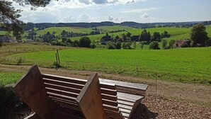 A bench in a rural setting with a view of green fields and distant hills.
