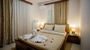 A hotel room with a bed, curtains, an air conditioner, a bedside table with a lamp, and a nightstand with a book.