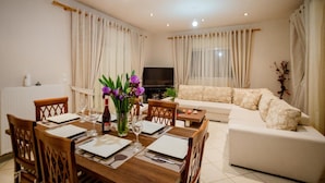 A living room with a dining table set for four, a sofa, a TV, and a plant.