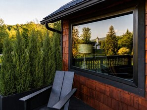 A modern outdoor seating area with a chair and a large window overlooking a forested landscape.
