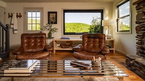 Uma sala de estar com dois poltronas de couro, uma mesa de centro, televisão e uma parede de pedra.