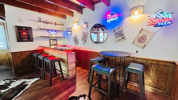 Una zona de bar con mostradores de madera, taburetes, letreros de neón y cuadros con naipes en la pared.