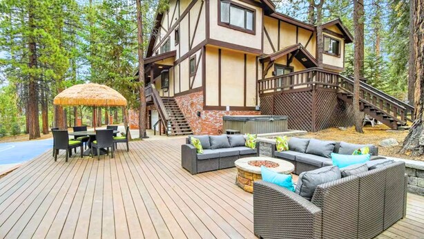 A wooden deck with outdoor furniture, a thatched umbrella, and a staircase leading to a second-story balcony.