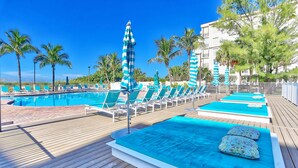 Ein Poolbereich mit Liegestühlen und Sonnenschirmen, einer Holzterrasse und einem klaren, blauen Pool.