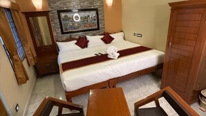 A hotel room with a bed, a wooden table, two chairs, a wardrobe, a mirror, and a stone wall with a painting. - Lake View Residency (Puducherry)