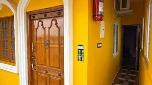 A hallway with a wooden door, yellow walls, and patterned floor tiles. - Lake View Residency (Puducherry)