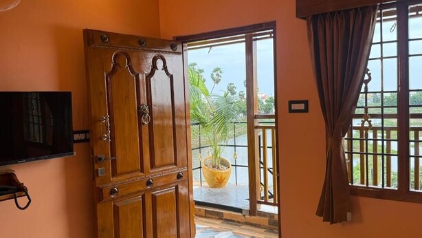A wooden door leading to a balcony with a potted plant and a view of palm trees. - Lake View Residency (Puducherry)