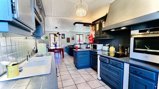 A modern kitchen with blue cabinets, a stainless steel oven, and a dining area with a table and chairs. - Family & Fun! Pedestrian center near Lake and Ski (Gérardmer)