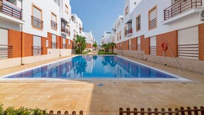 Una piscina rodeada de edificios modernos con balcones, cielo despejado y un flotador en el borde de la piscina.