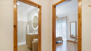 Habitación de hotel con marco de puerta de madera, baño con espejo y lavamanos, cama y una silla.