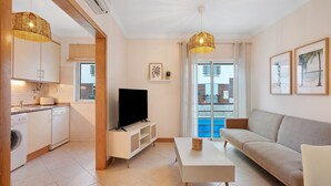 Una sala de estar moderna con sofá, mesa de centro, televisor y área de cocina con electrodomésticos.