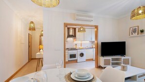 Una cocina moderna con electrodomésticos blancos, un comedor con una mesa dispuesta para dos personas y un televisor sobre un mueble.