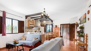 Un'ampia zona giorno con divano, tavolo da pranzo e sedie, una cucina con travi in legno e vista attraverso una porta scorrevole.