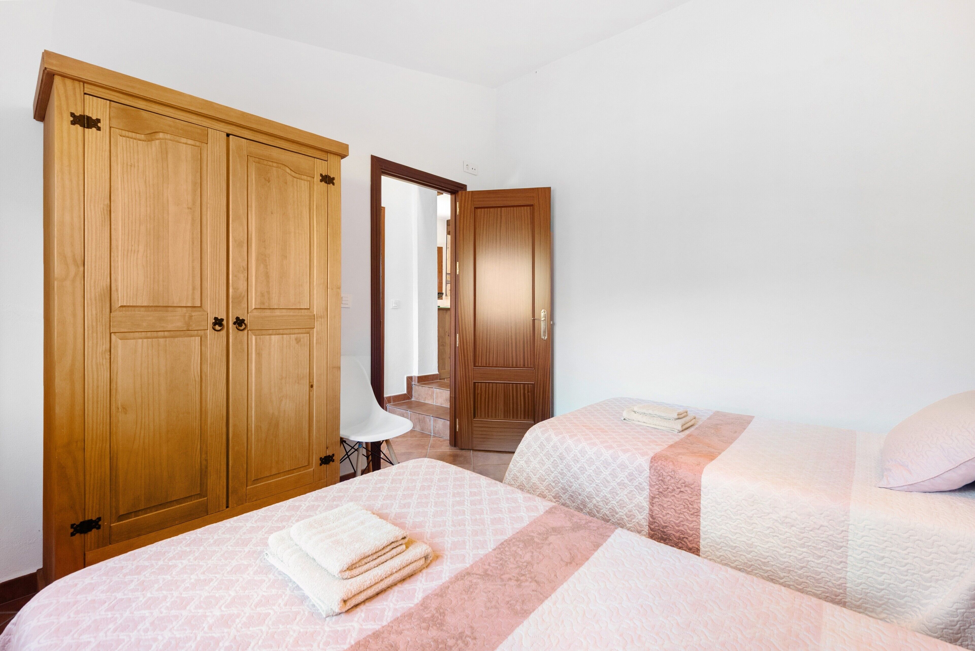Un dormitorio con dos camas, armarios de madera, una silla y una puerta que da a otra habitación.