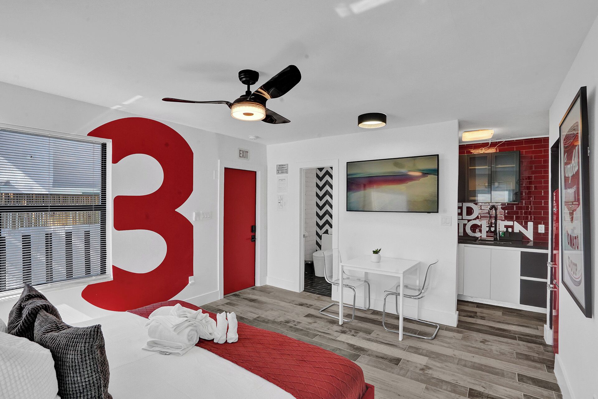A modern hotel room with a large '31' sign, a ceiling fan, a small dining area, and a kitchen visible through a glass partition.