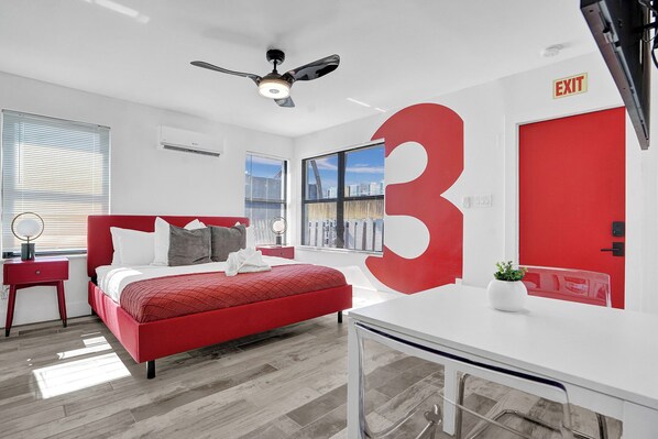 A modern hotel room with a large red number '3' on the wall, a bed with red bedding, a desk, and a ceiling fan. - Gorgeous studio just a stone's throw from the beach (Hollywood)