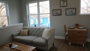 A living room with a sectional sofa, a wooden coffee table, and a dining area with a wooden table set for two. - Charming DC Carriage House: Perfect for Couples, Small Families Weekend Trips (Washington DC)
