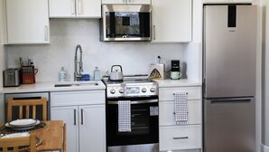 A modern kitchen with white cabinets, a stainless steel microwave, a built-in oven, a refrigerator, and a wooden dining table with chairs. - Charming DC Carriage House: Perfect for Couples, Small Families Weekend Trips (Washington DC)