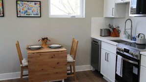 A kitchen with white cabinets, a stainless steel microwave, a dishwasher, and a wooden dining table with chairs. - Charming DC Carriage House: Perfect for Couples, Small Families Weekend Trips (Washington DC)
