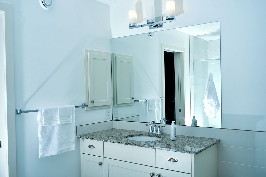 A bathroom with a granite countertop sink, a large mirror, and a towel rack.