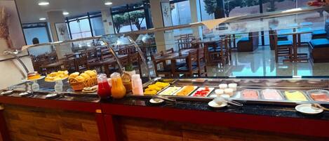 A buffet with various food items and beverages, a glass partition, and wooden furniture.