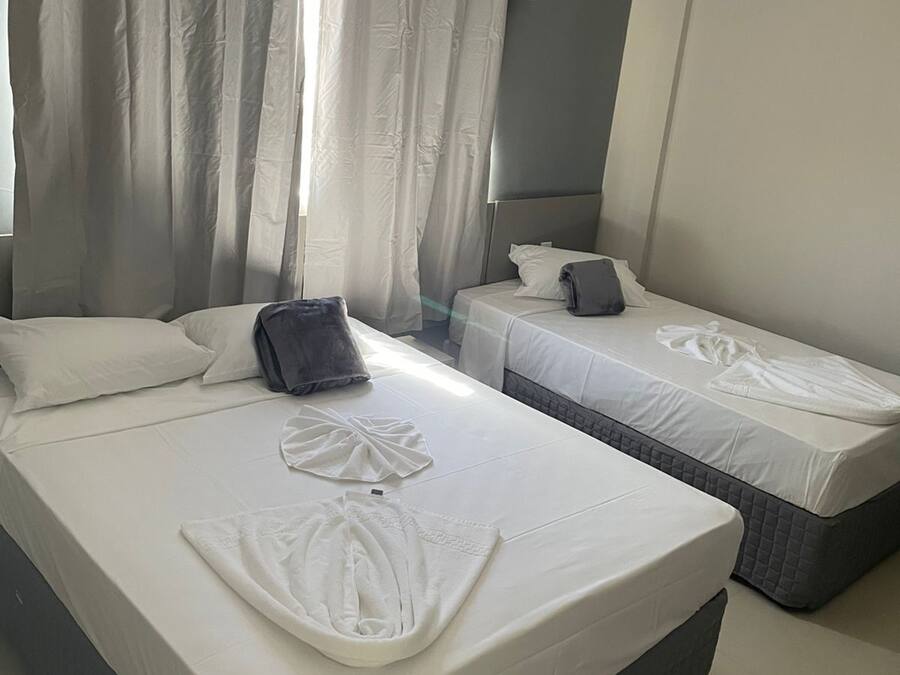 A hotel room with two beds, a grey headboard, and a large window with curtains.