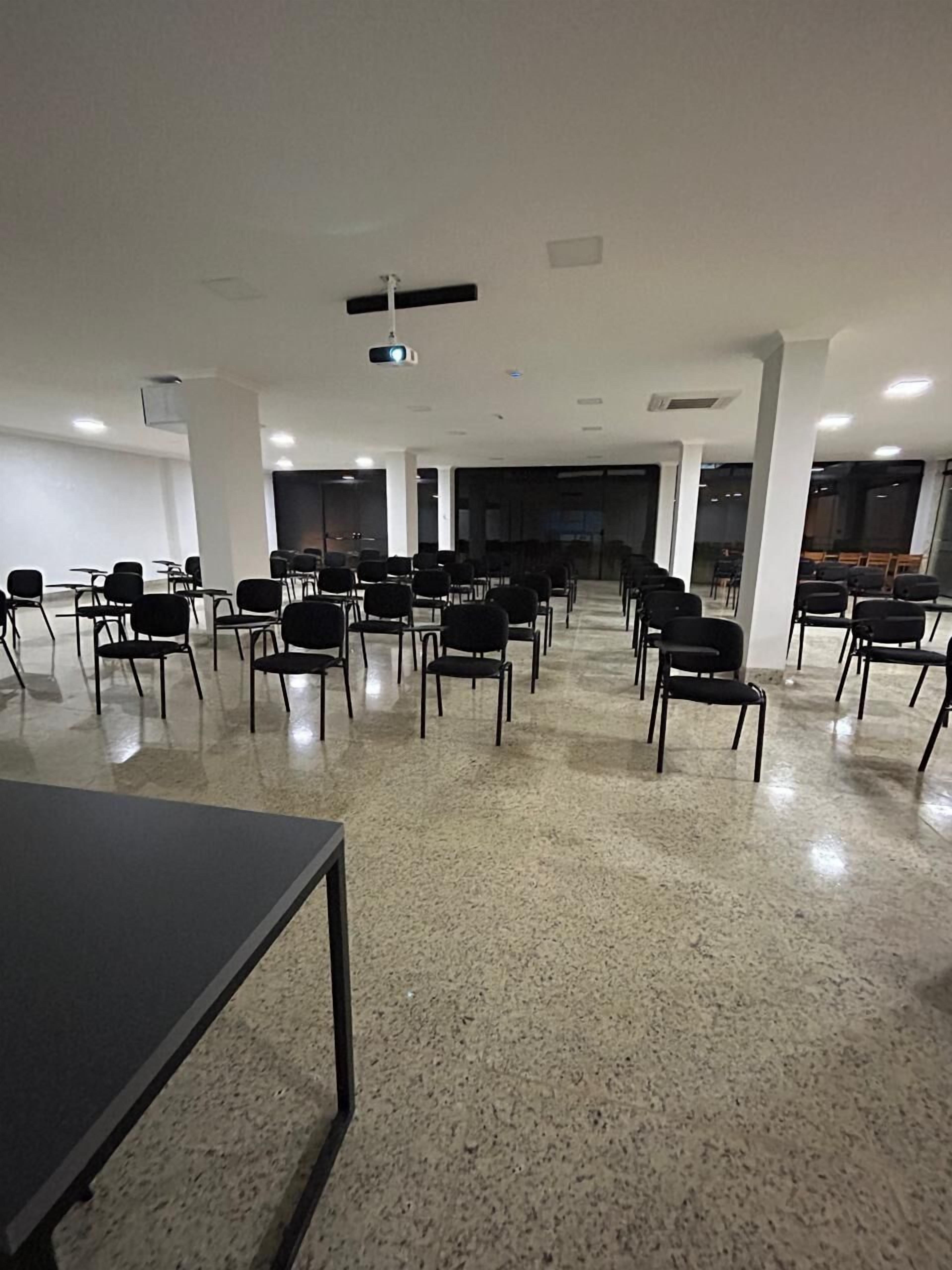 Un salón de conferencias con filas de sillas, un proyector y una pantalla grande.