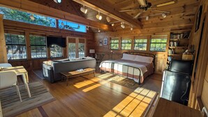 A cozy cabin interior with a sofa, bed, dining table, and a refrigerator. - Hill Country Retreat (Austin)