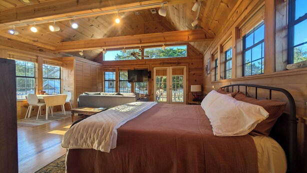 A wooden cabin interior with a large bed, a desk, and a sofa. - Hill Country Retreat (Austin)