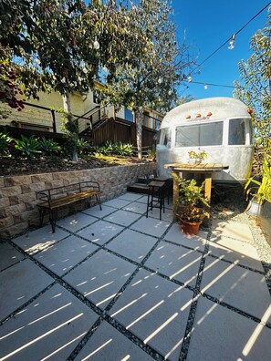 A vintage trailer with a table and chairs, surrounded by a garden with plants and a stone patio. - Awesome 2-bedroom caravan with AC in charming Spring Valley (Spring Valley)