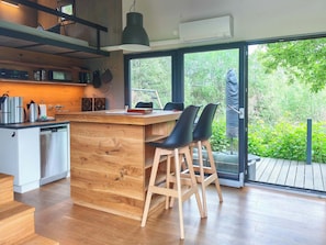 Une cuisine moderne avec un îlot central en bois, des tabourets de bar et une grande fenêtre donnant sur un espace verdoyant.