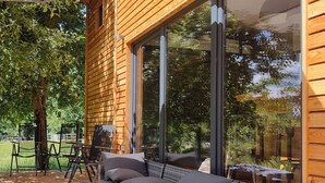 A modern outdoor seating area with a sofa and chairs, large windows, and a wooden deck. - Spacious tiny house with a large terrace, ideal for families – Last Minute (Großharthau)