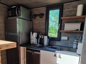 Eine kompakte Küche mit integriertem Mikrowellenherd, Kühlschrank, Geschirrspüler, einem Fenster mit Blick auf Grünflächen und einer kleinen Ablage mit Küchenpapier.