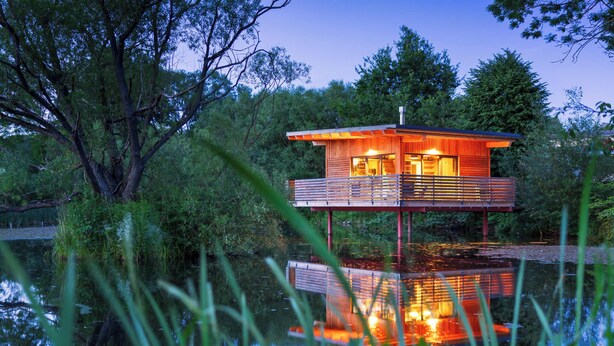 Une cabane en bois sur pilotis, au-dessus de l’eau, entourée d’arbres.