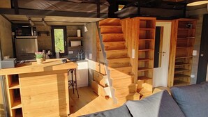 Une cuisine compacte avec un coin bar, un escalier en bois et un espace détente avec des coussins.