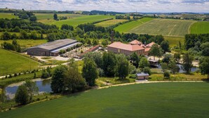 Un paysage rural avec un vaste ensemble de bâtiments, entouré de champs et d’un petit plan d’eau.